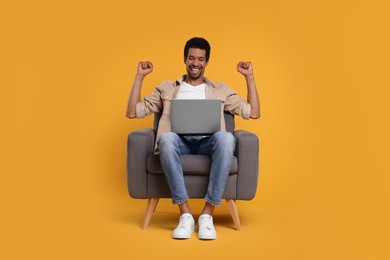 Emotional man with laptop sitting in armchair on orange background