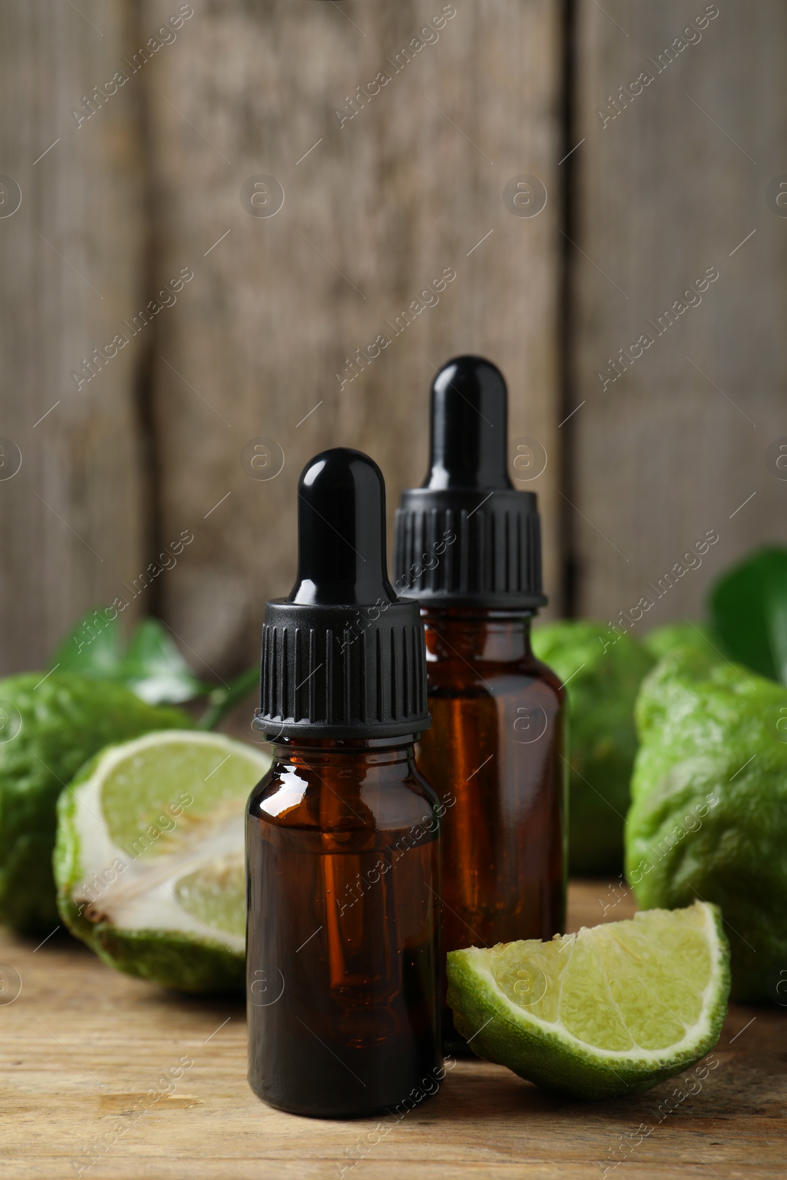 Photo of Bottles of essential oil and fresh bergamot fruits on wooden table