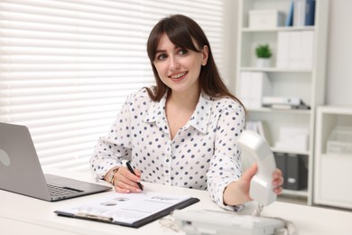 Smiling secretary taking telephone handset at table in office