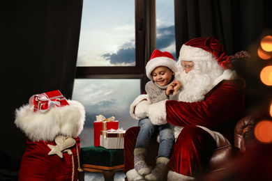 Photo of Santa Claus with little boy near window indoors. Christmas time