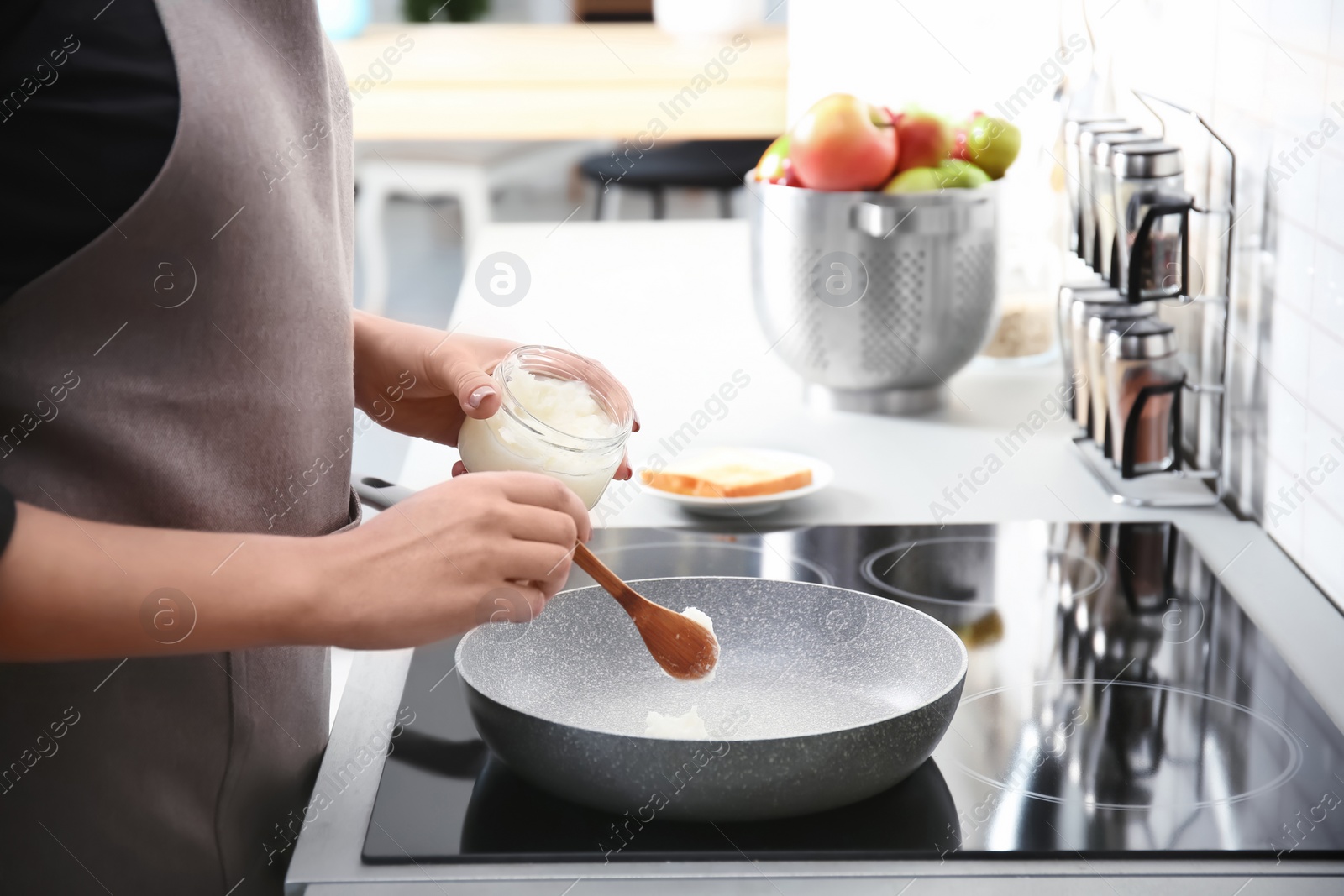 Photo of Woman putting coconut oil on frying pan in kitchen, closeup