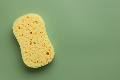New yellow sponge on green background, top view. Space for text