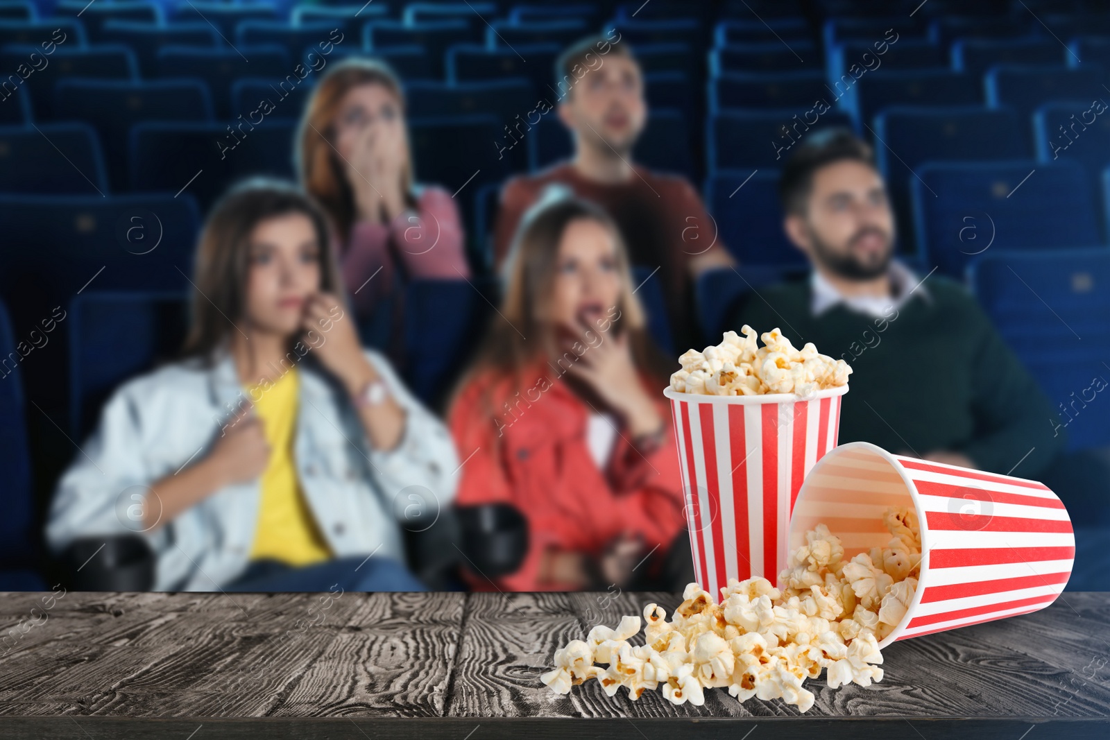 Image of Popcorn on table and young people in cinema hall, space for text  