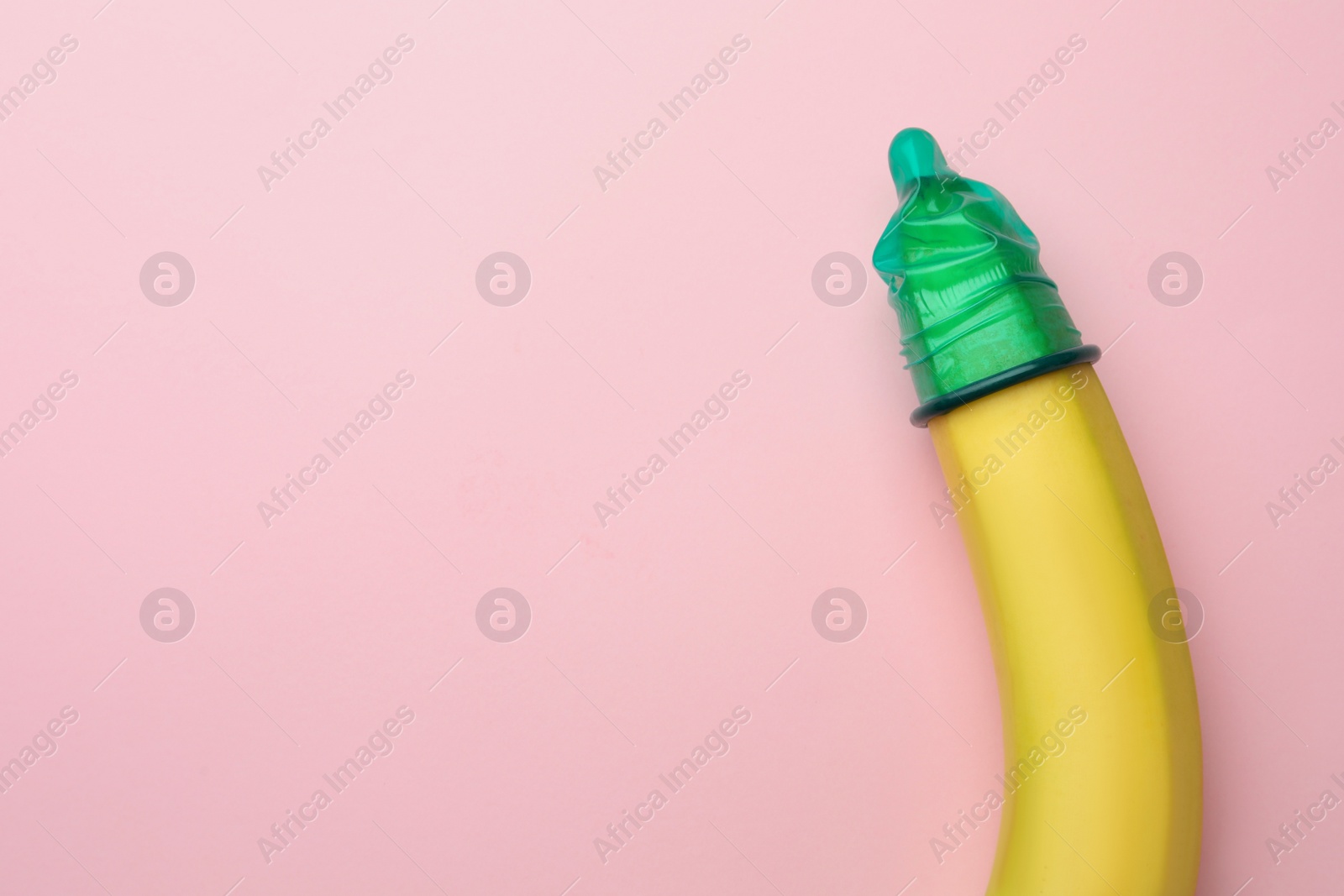 Photo of Banana with condom on pink background, top view and space for text. Safe sex concept