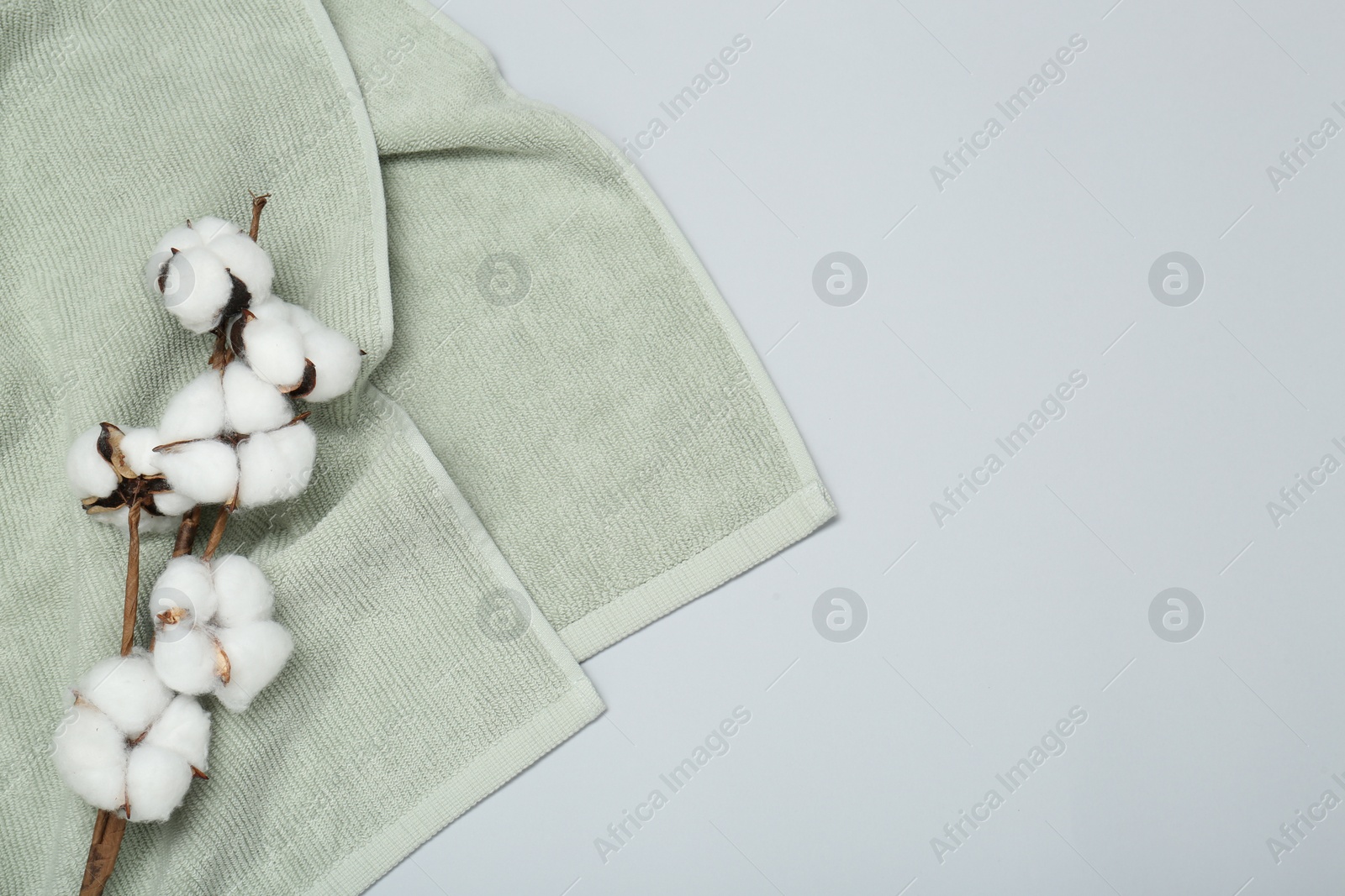 Photo of Soft green towel and cotton flowers on light grey background, top view. Space for text
