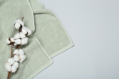 Soft green towel and cotton flowers on light grey background, top view. Space for text