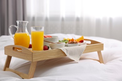 Photo of Wooden tray with tasty breakfast on bed at home