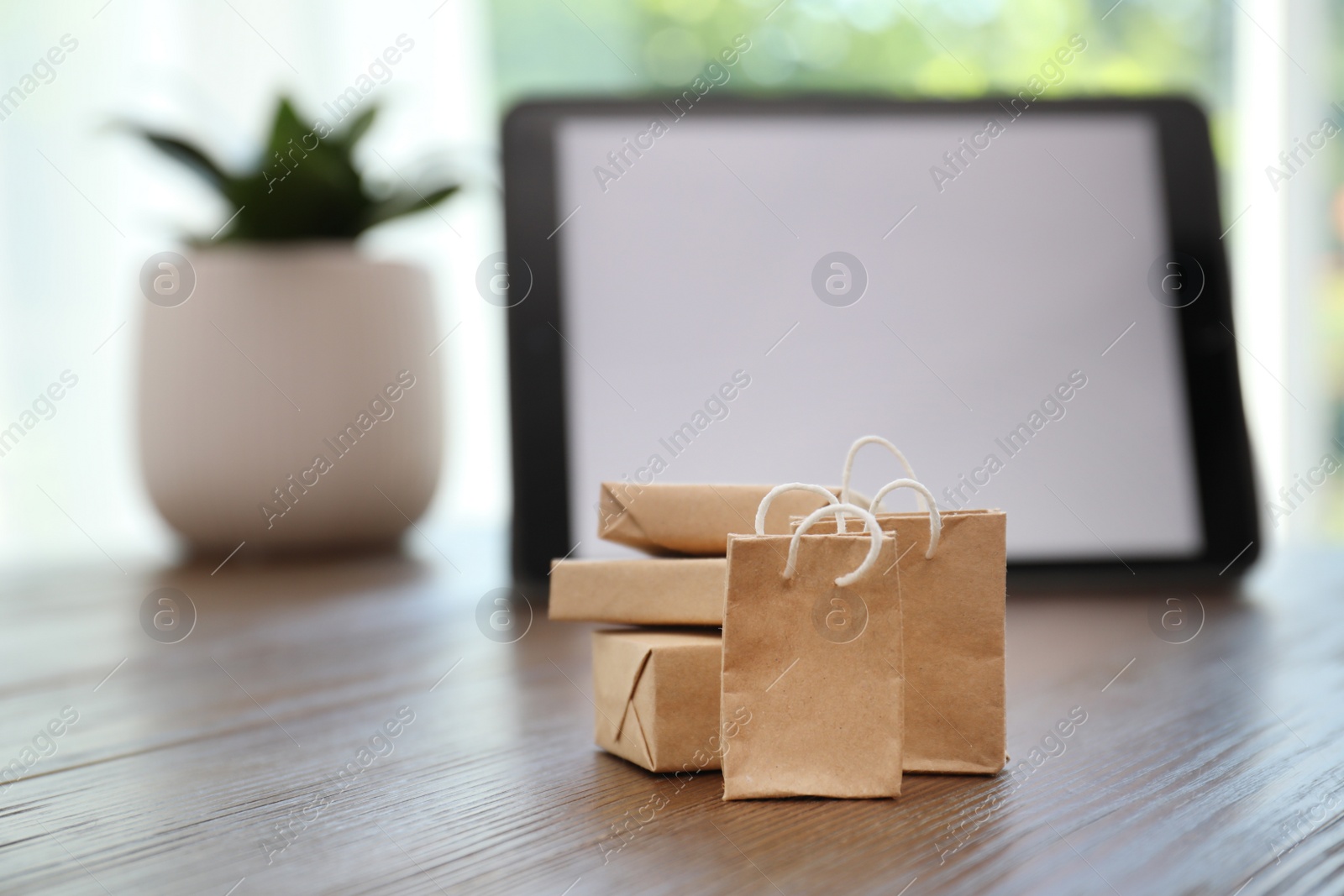 Photo of Internet shopping. Small bags and boxes near modern tablet on table indoors, space for text