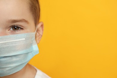 Cute little girl in protective mask on yellow background, closeup. Space for text