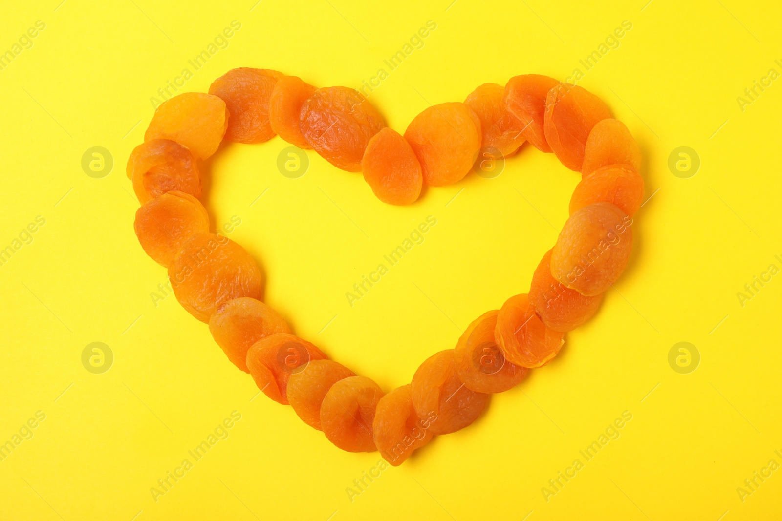 Photo of Heart shaped frame made of dried apricots on color background, top view with space for text. Healthy fruit