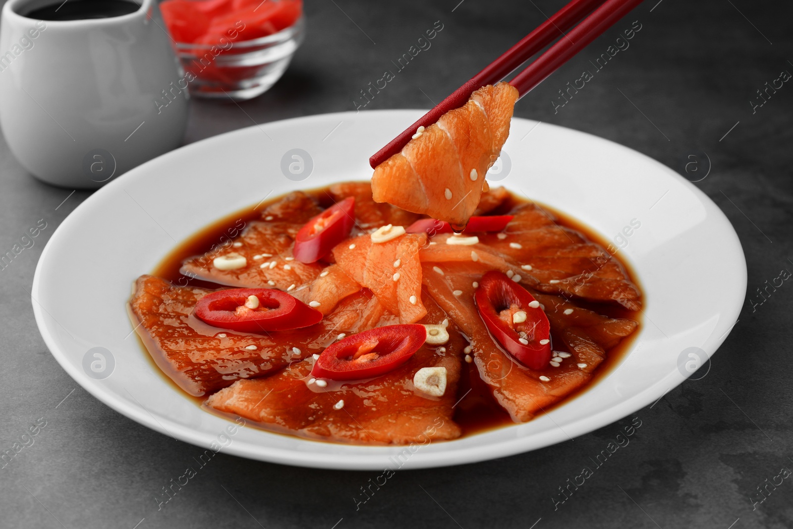 Photo of Taking tasty sashimi from plate at grey table, closeup