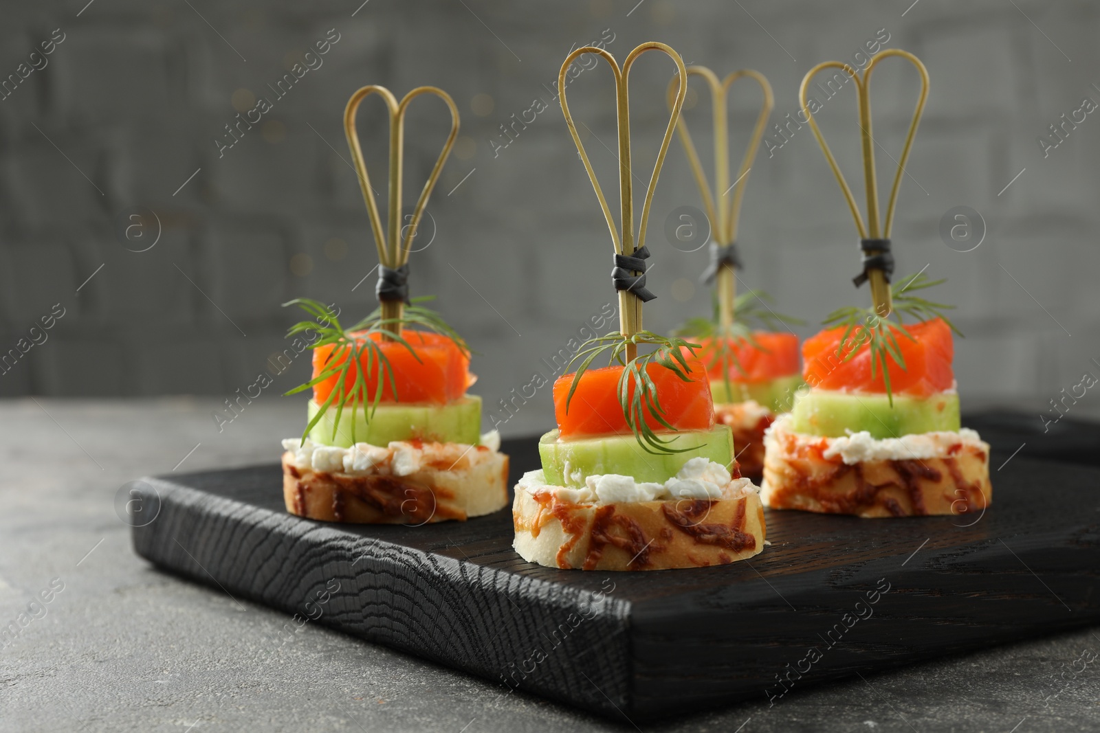 Photo of Tasty canapes with salmon, cucumber, bread and cream cheese on grey table, closeup