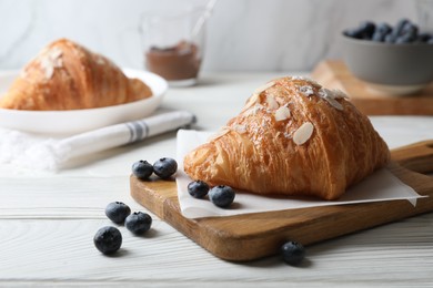 Photo of Delicious croissant with almond flakes and blueberries on white wooden table, closeup