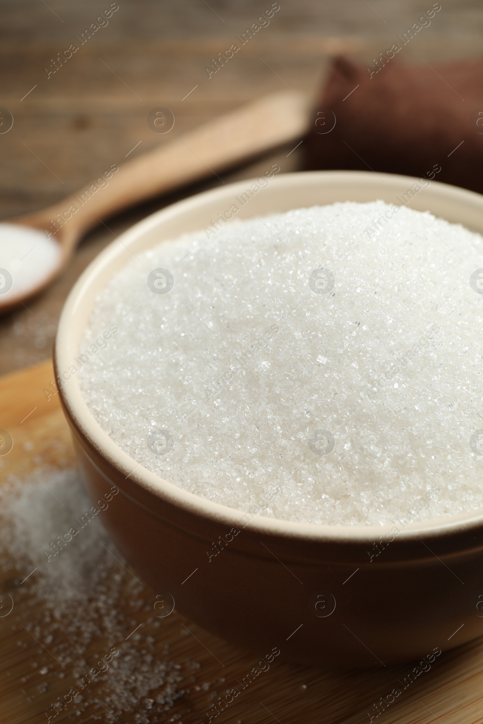 Photo of Granulated sugar in bowl on wooden table, closeup