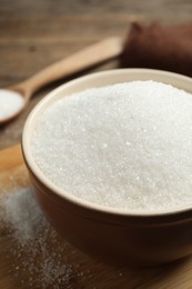 Granulated sugar in bowl on wooden table, closeup