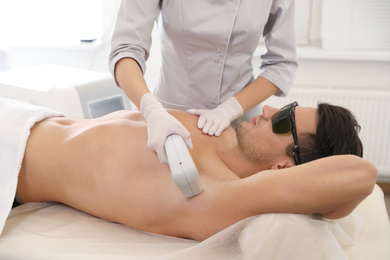 Photo of Young man undergoing laser epilation procedure in beauty salon