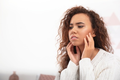 Photo of African-American woman suffering from tooth ache indoors. Space for text