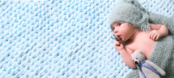 Image of Cute baby baby with pacifier and crochet toy on light blue blanket, top view. Banner design with space for text