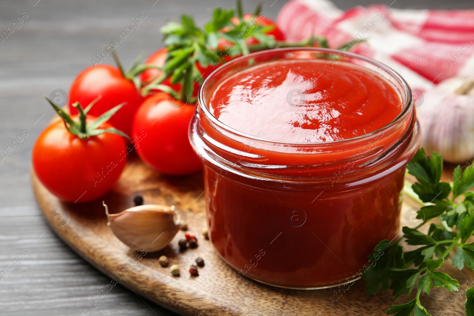 Photo of Tasty ketchup, fresh tomatoes, parsley and spices on grey wooden table