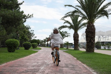 Photo of Young woman riding bicycle on lane outdoors, back view