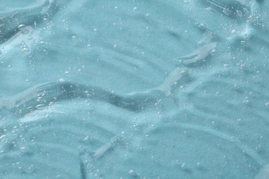 Clear cosmetic serum on light blue background, macro view