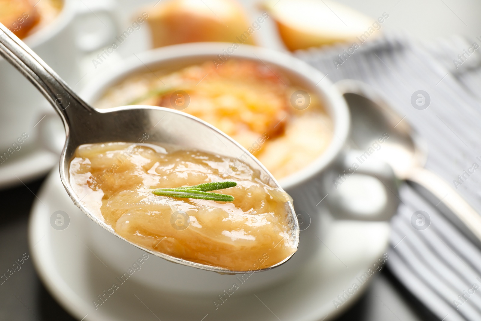 Photo of Spoon with fresh homemade homemade french onion soup over bowl, closeup