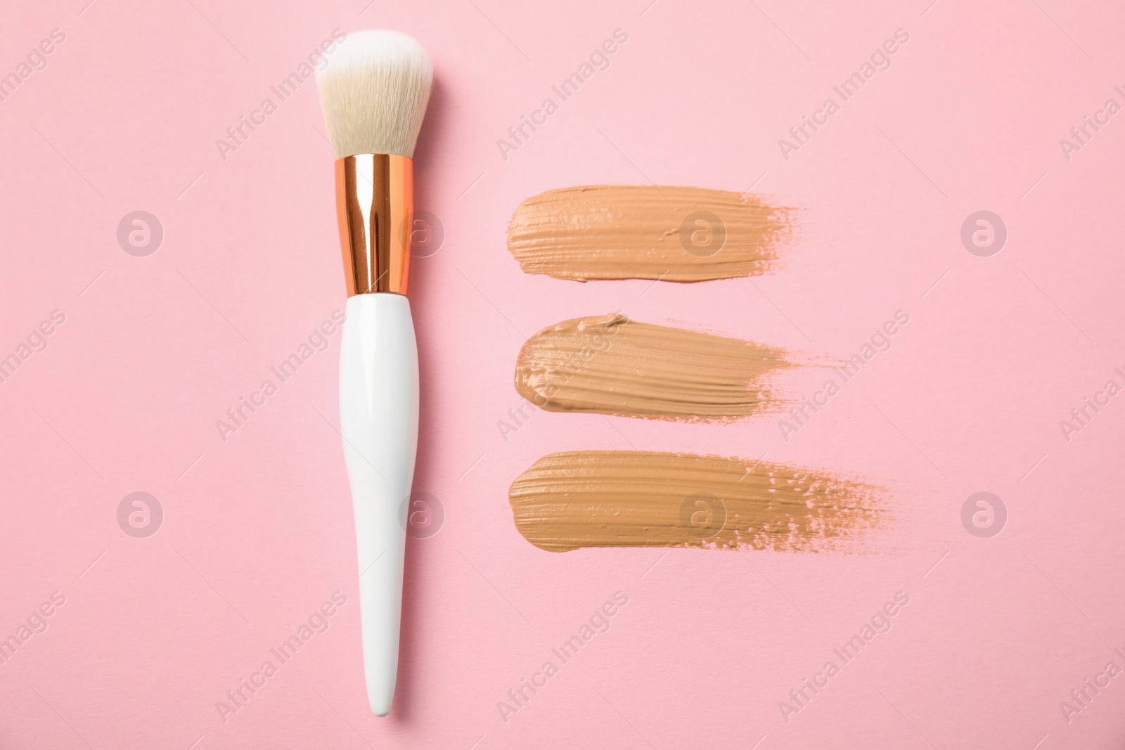 Photo of Samples of different foundation shades and makeup brush on pink background, above view