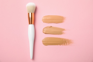Samples of different foundation shades and makeup brush on pink background, above view