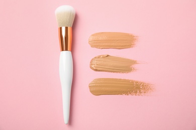 Photo of Samples of different foundation shades and makeup brush on pink background, above view