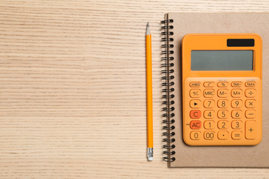 Photo of Calculator, notebook and pencil on wooden table, top view with space for text. Tax accounting