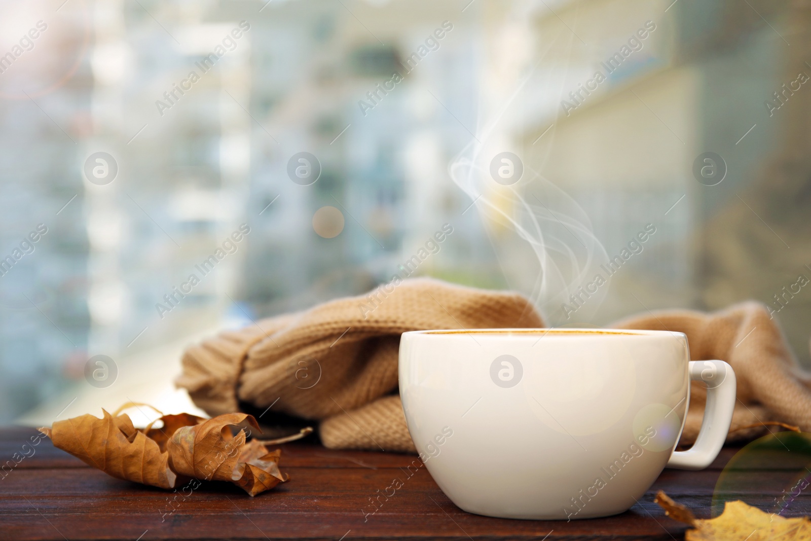 Image of Cup of hot coffee and autumn leaves on window sill indoors. Space for text