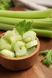 Photo of Bowl with fresh green cut celery on wooden table, closeup