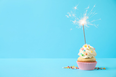 Photo of Birthday cupcake with sparkler on light blue background. Space for text