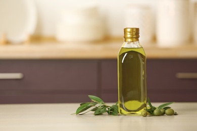 Bottle of oil and olive tree twig on table against blurred background. Space for text