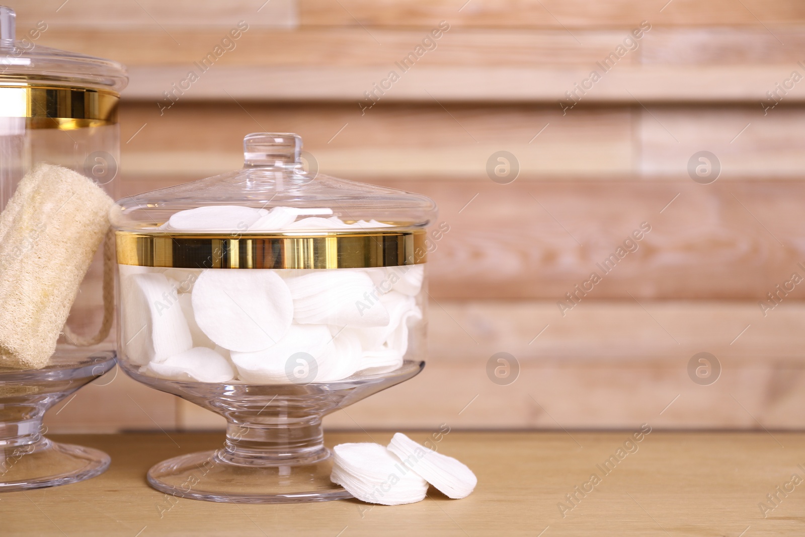 Photo of Glass jar with cotton pads on table near wooden wall. Space for text
