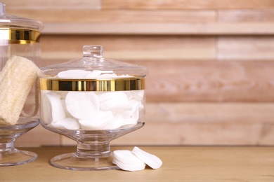 Glass jar with cotton pads on table near wooden wall. Space for text