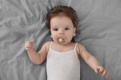 Photo of Cute little baby with pacifier on bed, top view