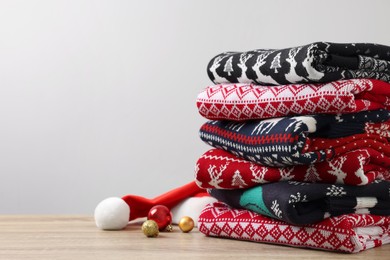 Photo of Stack of different Christmas sweaters, Santa hat and baubles on wooden table against light background. Space for text