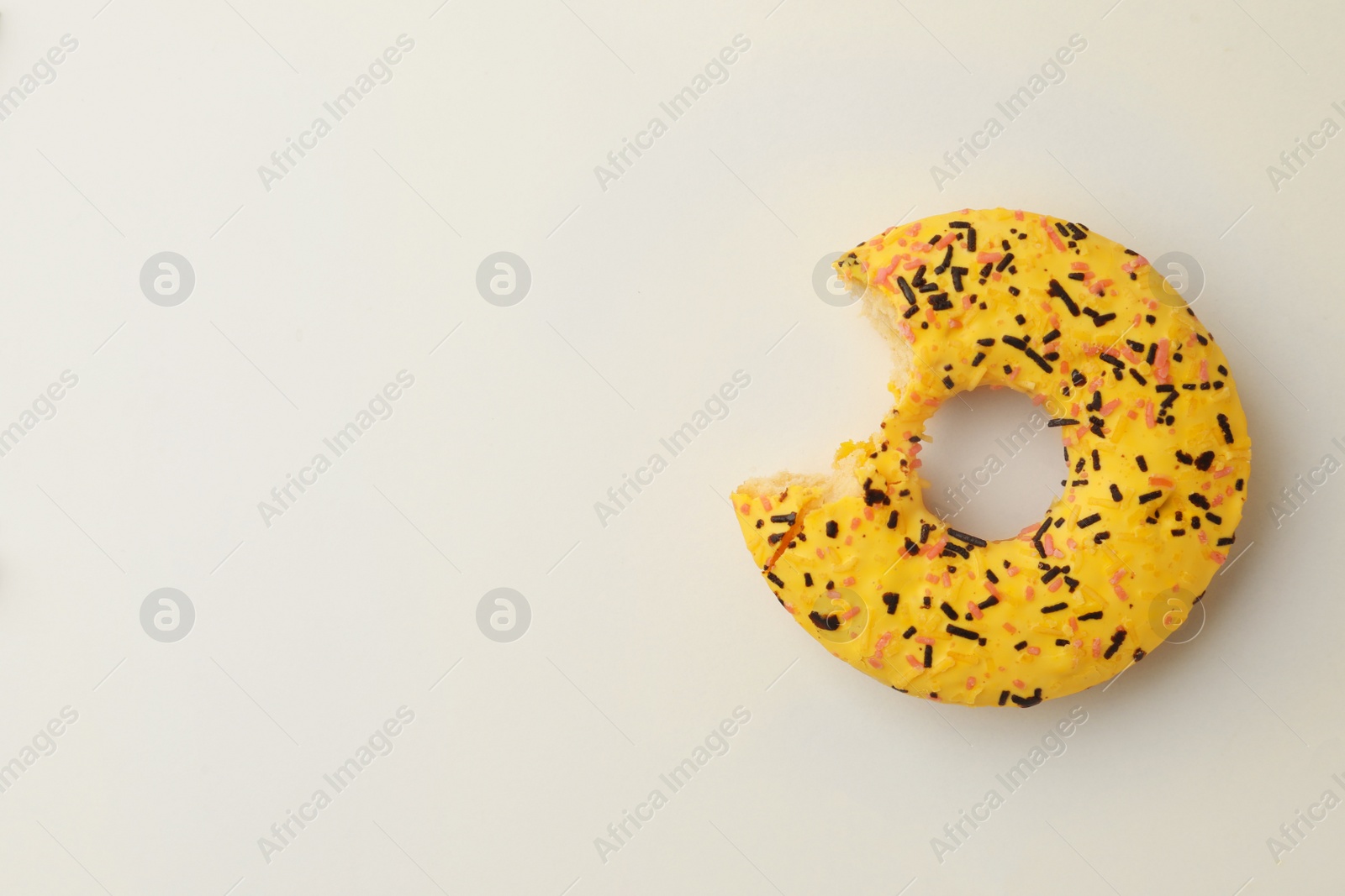 Photo of Delicious yellow glazed donut with bite mark on white background, top view. Space for text