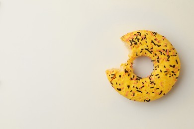 Delicious yellow glazed donut with bite mark on white background, top view. Space for text