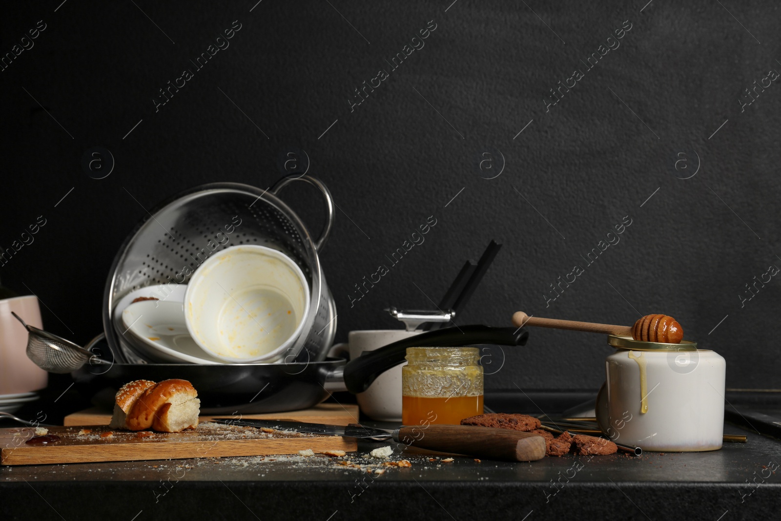 Photo of Many dirty utensils, dishware and food leftovers on black countertop. Mess in kitchen