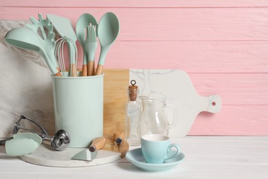 Set of different kitchen utensils on white table against pink wooden background, space for text