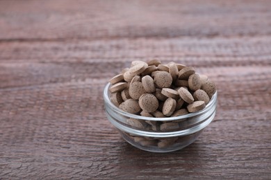 Brewer's yeast tablets in bowl on wooden table, space for text