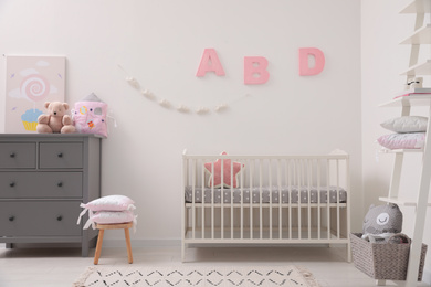 Photo of Cute baby room interior with crib and chest of drawers near white wall