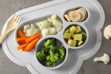 Photo of Baby food. Section plate with different vegetables and bananas served on grey textured table, flat lay