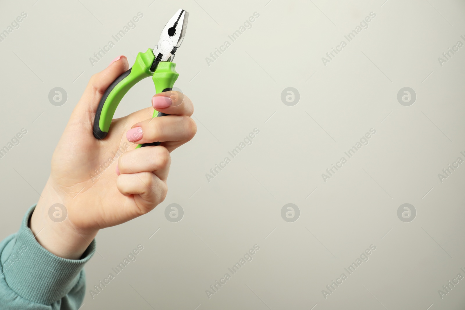 Photo of Woman with combination pliers on grey background, closeup. Space for text