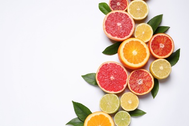 Photo of Fresh juicy citrus fruits with green leaves on white background, flat lay. Space for text