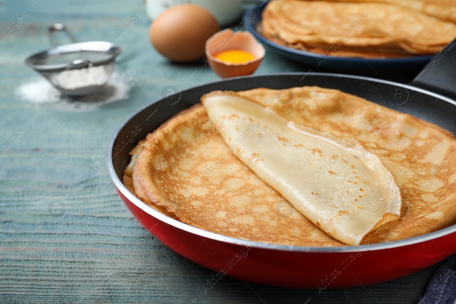 Photo of Delicious thin pancakes on blue wooden table, closeup