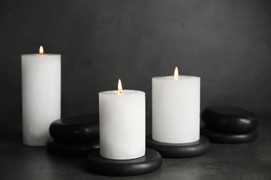 Photo of Burning candles and black spa stones on grey table