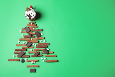 Photo of Christmas tree made with marshmallows, cinnamon and chocolate on green background, flat lay. Space for text